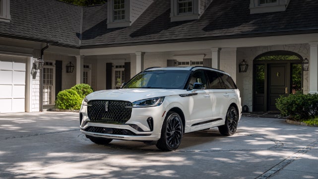 A white 2026 Lincoln Aviator® SUV is parked in the driveway of a luxury home. | Crest Lincoln in Sterling Heights MI