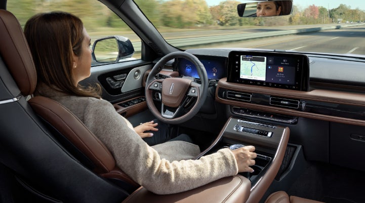 A 2027 Lincoln Aviator® SUV is being driven hands-free on a highway lined with trees. | Crest Lincoln in Sterling Heights MI