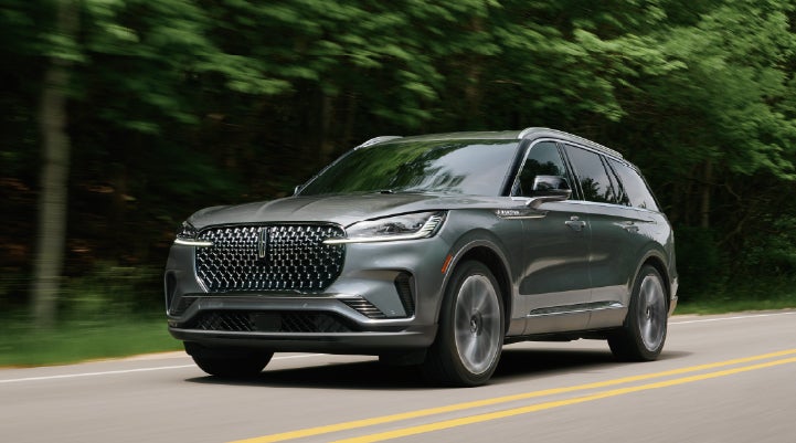 A 2027 Lincoln Aviator® SUV is being driven down a road lined with trees. | Crest Lincoln in Sterling Heights MI