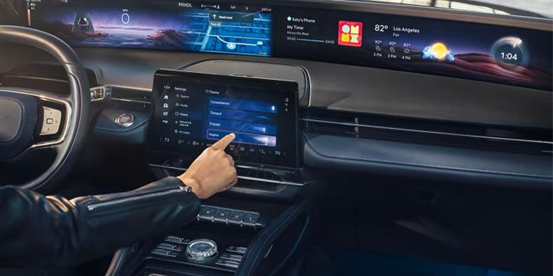 Car interior with wide screen dashboard and hand touching center display