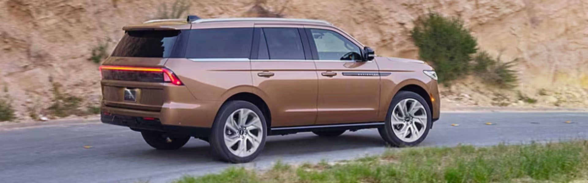 Bronze SUV driving on a road next to a rocky hill